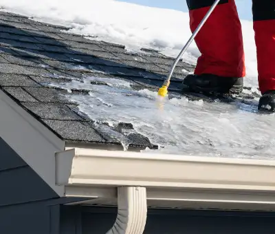 Ice dam removal technician using a steam wand to melt thick ice buildup on a residential roof in Nashville, TN