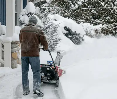 Residential snow removal technician using a snow blower to clear a home driveway and walkway in Nashville, TN